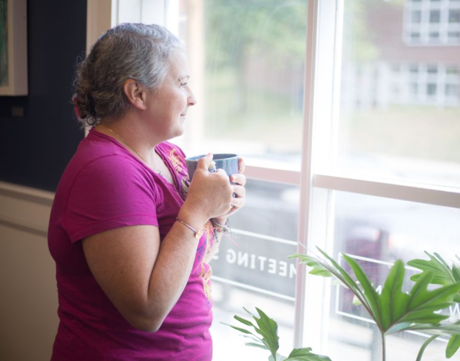 Une femme se tient près d’une fenêtre, une tasse à la main